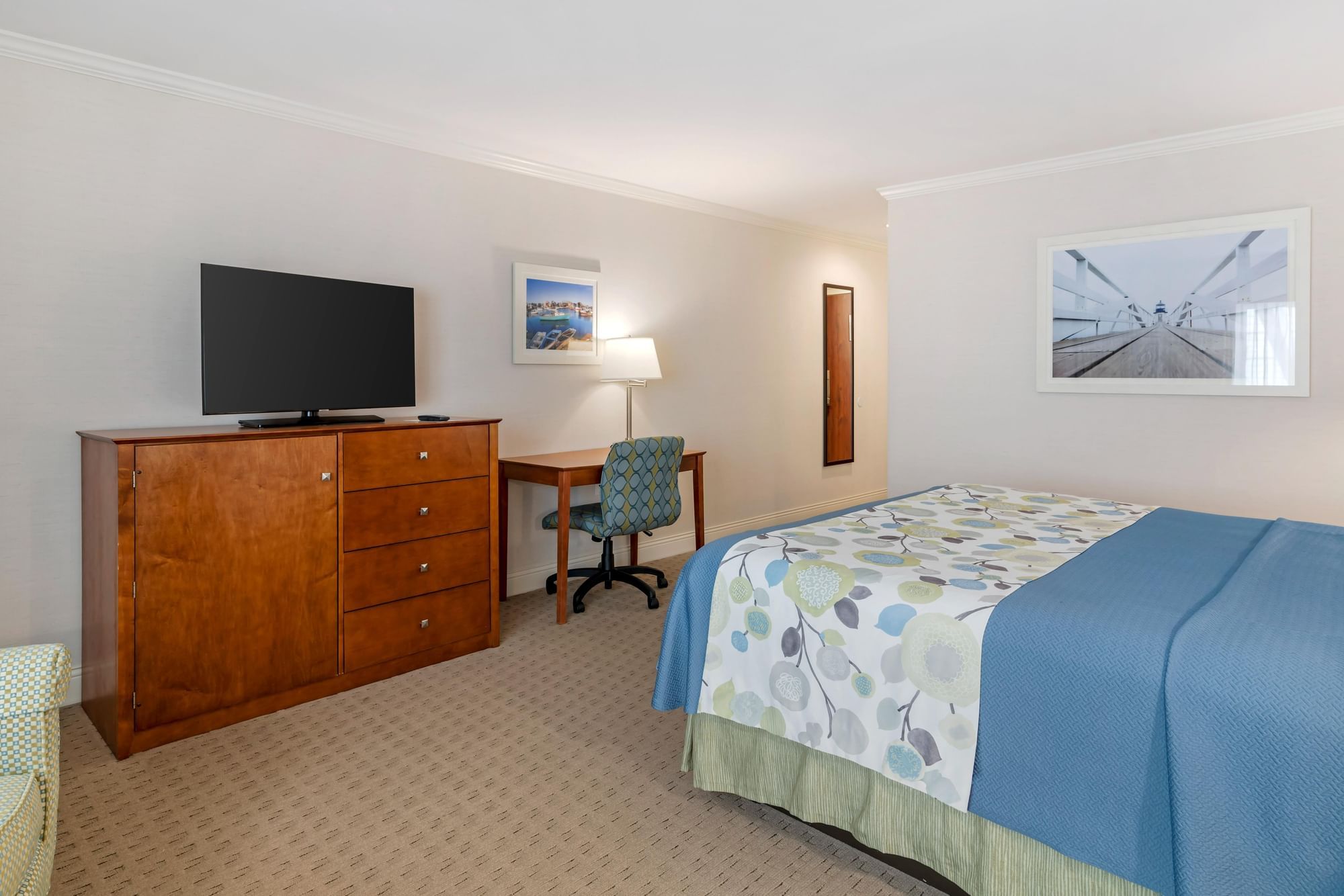 A hotel room with a bed, desk, dresser, and TV