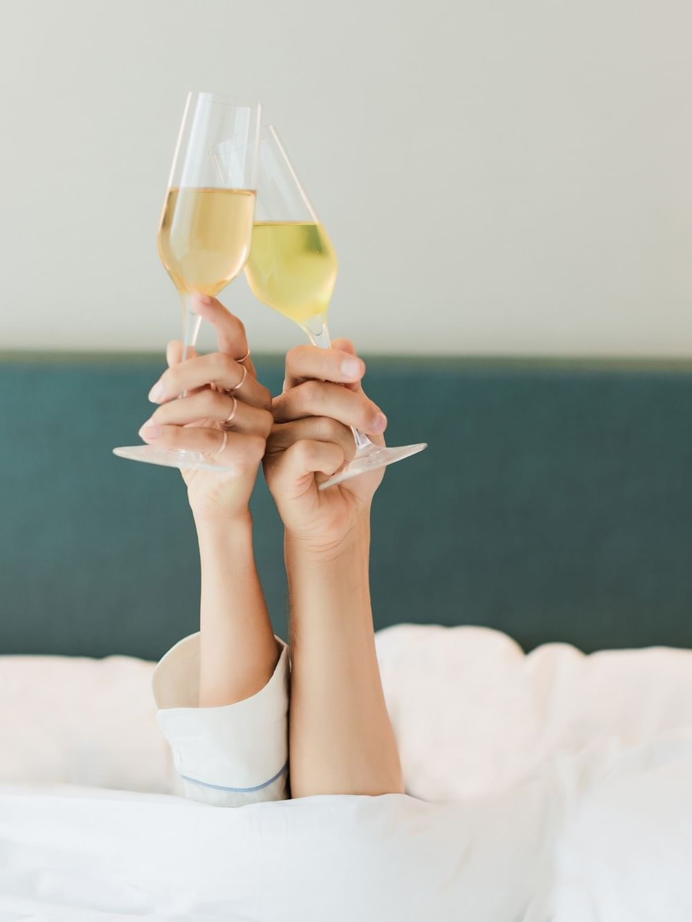 Hands raising wine glasses by a dark headboard under a white duvet at Warwick San Francisco