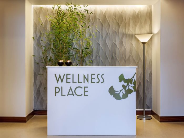 Front desk with standing lamp & sign featuring Wellness Place in the spa reception at Bensaude Hotels Collection