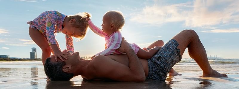 Father and two young girls enjoying a day at the beach in the Get Up and Gold Coast offer.