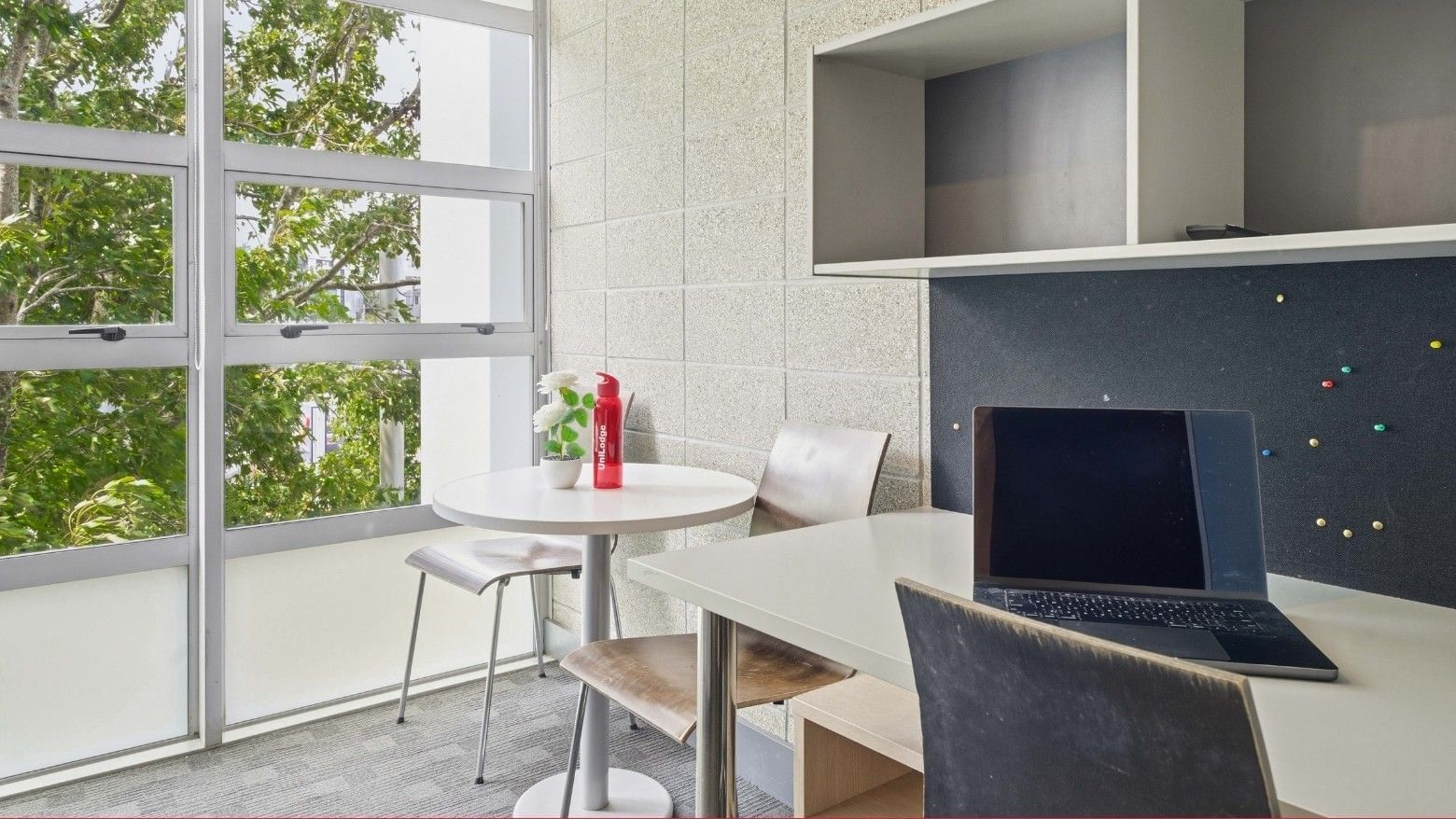 Laptop on a desk with a round table and chairs near large windows at Student Living Auckland - Beach.