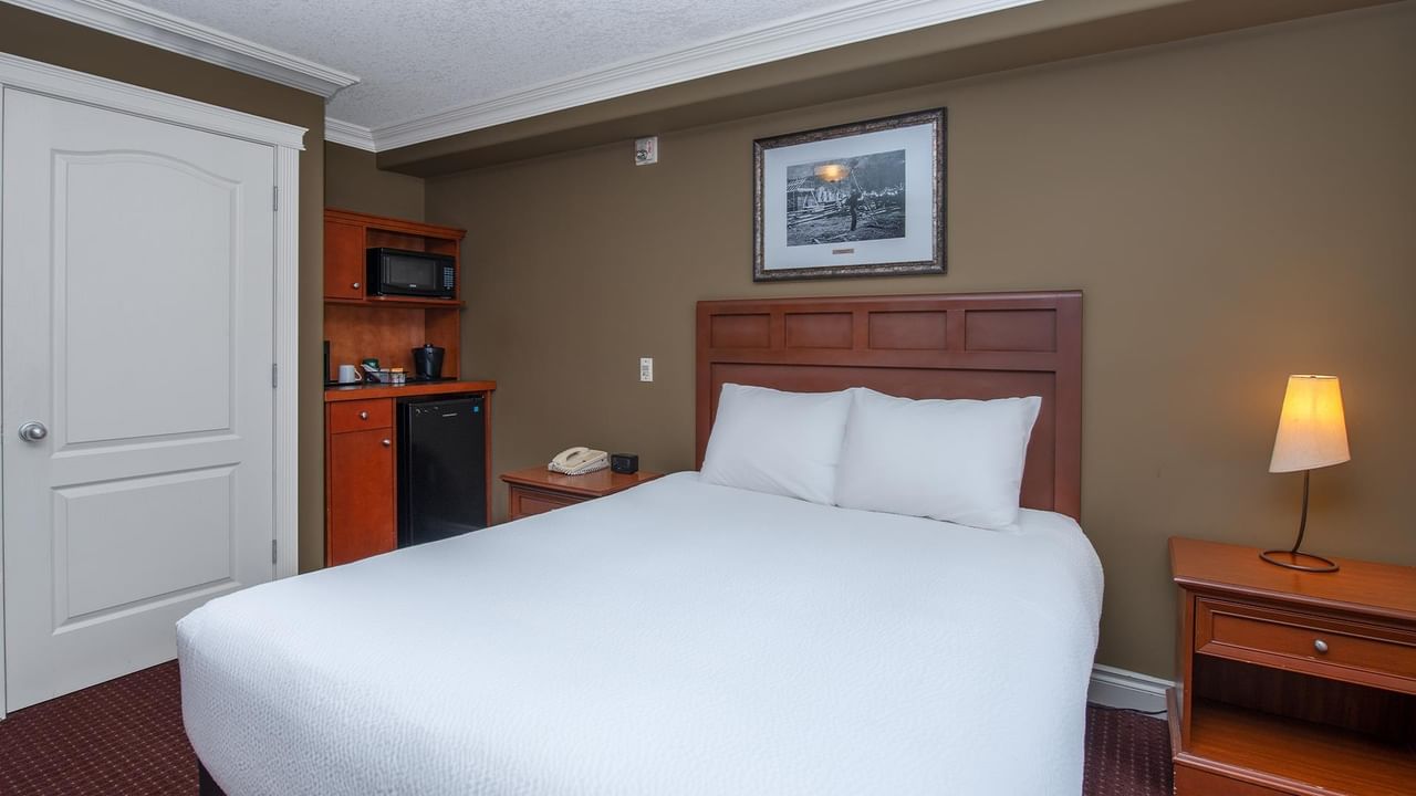 Guest room with white bedding, wooden headboard, kitchenette, and bedside lamp at Coast Edson Hotel.