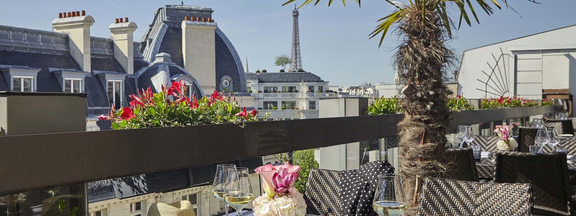 Dining tables arranged on a balcony overlooking the Eiffel Tower from Warwick Paris Champs Elysées