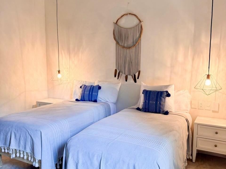Two beds with blue blankets and pillows in a room with white walls and hanging decorations.