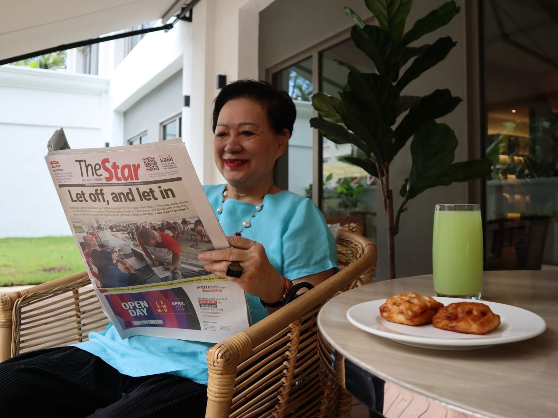 A woman sitting in a chair reading a newspaper at MiCasa All Suite Hotel KL