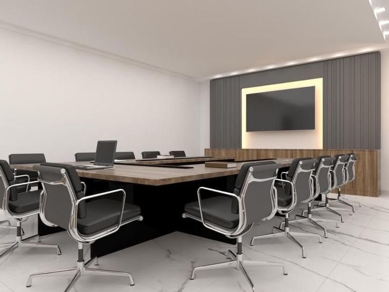 Black leather chairs by a wooden table under a large wall-mounted monitor in Orchid 1 at Cantonal Hotel by Warwick Riyadh