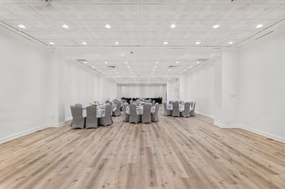 Modern ballroom at The Riverwalk Plaza Hotel with wood flooring, gray tables, and ample space under bright ceiling lights