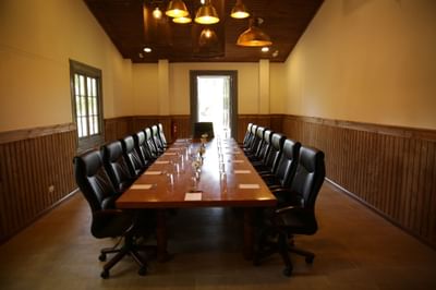 Long wooden table by black leather chairs under hanging gold lamps in Merlot Salon at NOI Blend Colchagua