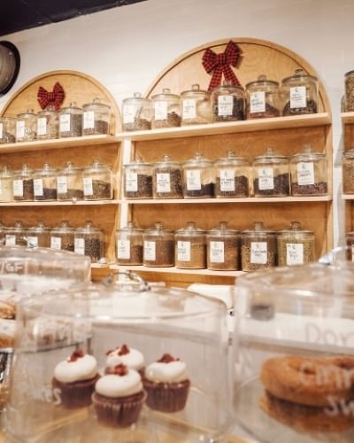 A wall of arched displays of glass jars of tea with glass cake stands and pastries in the foreground. Infusion Tea is a wonderful tea room in Orlando.