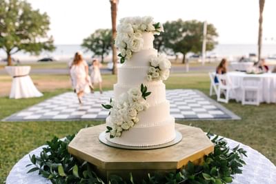 Five-tier white wedding cake adorned with fresh roses at an outdoor lawn event inside The White House Hotel