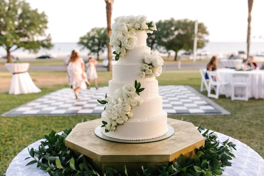 Five-tier white wedding cake adorned with fresh roses at an outdoor lawn event inside The White House Hotel