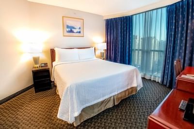 Suite featuring cozy bed and floor-to-ceiling dark blue drapes at Rosedale on Robson Suite Hotel