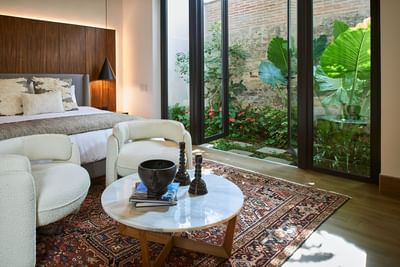 Casa Campanas bedroom with two armchairs, a marble table, and a view of a lush garden at Singular Signature Residences
