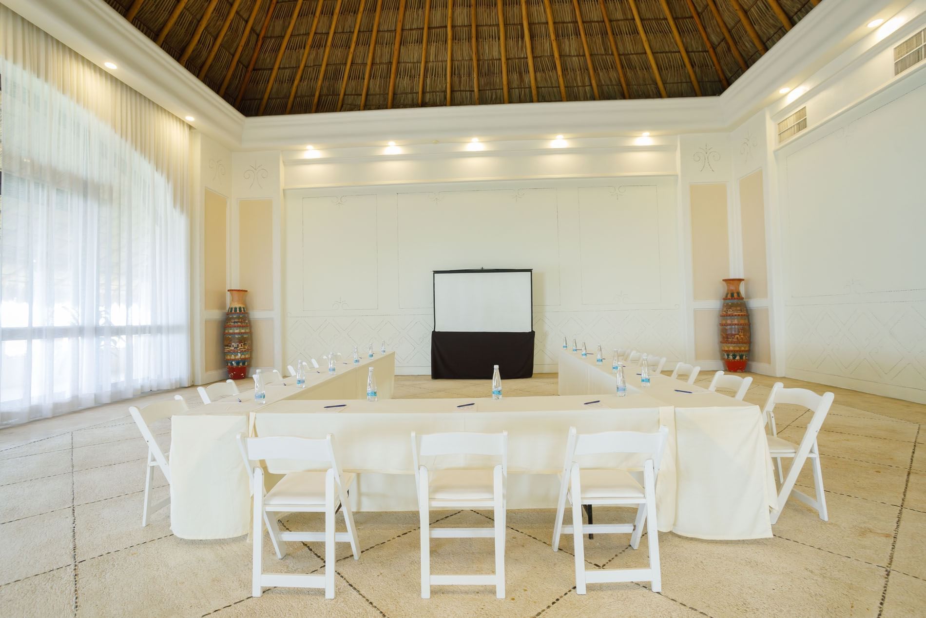 U-shaped Ixtac Venue with white chairs, bottled water, and a projector screen at Quinta Real Acapulco