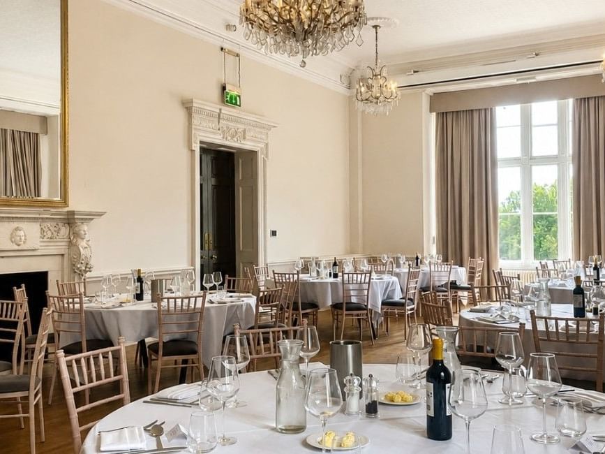 Elegant Downshire Ballroom with crystal chandeliers, round tables set for dining, and tall windows at Easthampstead Park Hotel