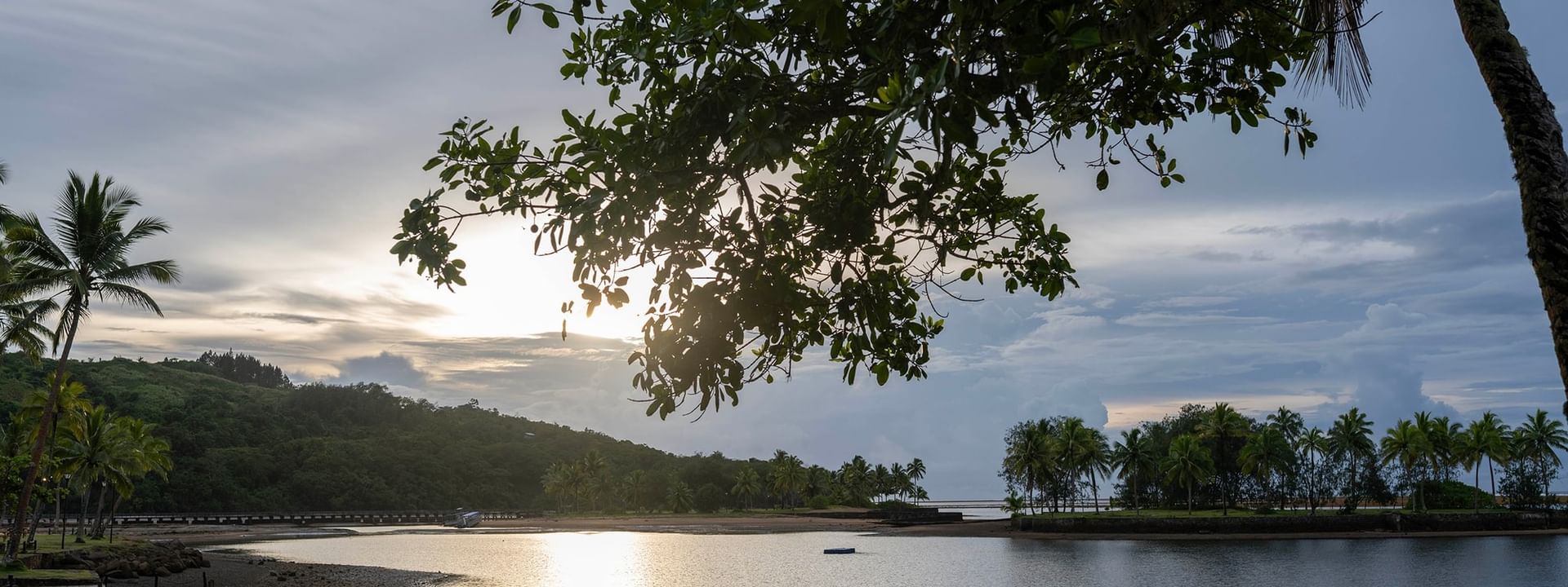 Calm coastal inlet by a sandy shore under a leafy tree branch at The Naviti Resort