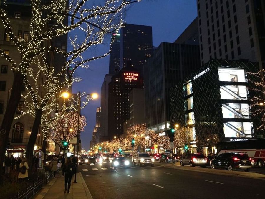 Busy city street with holiday lights, placed by the glowing signage of the Warwick Allerton Chicago at night