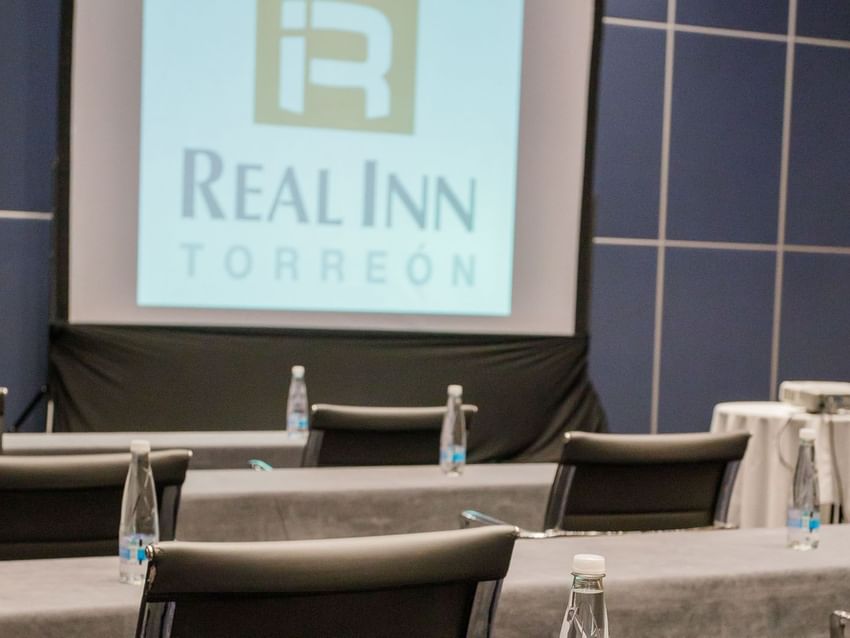 Paris meeting room with a projector screen, grey tables, and bottled water setup at Real Inn Torreon
