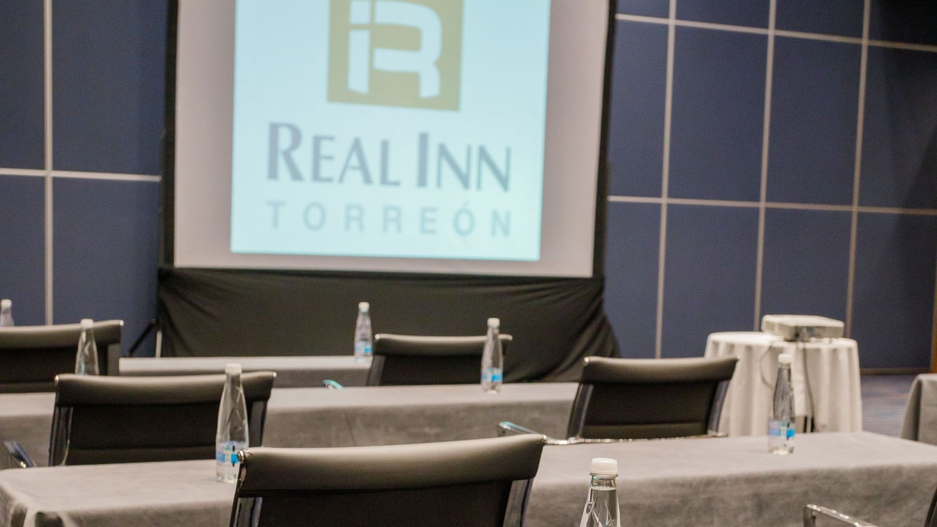Paris meeting room with a projector screen, grey tables, and bottled water setup at Real Inn Torreon