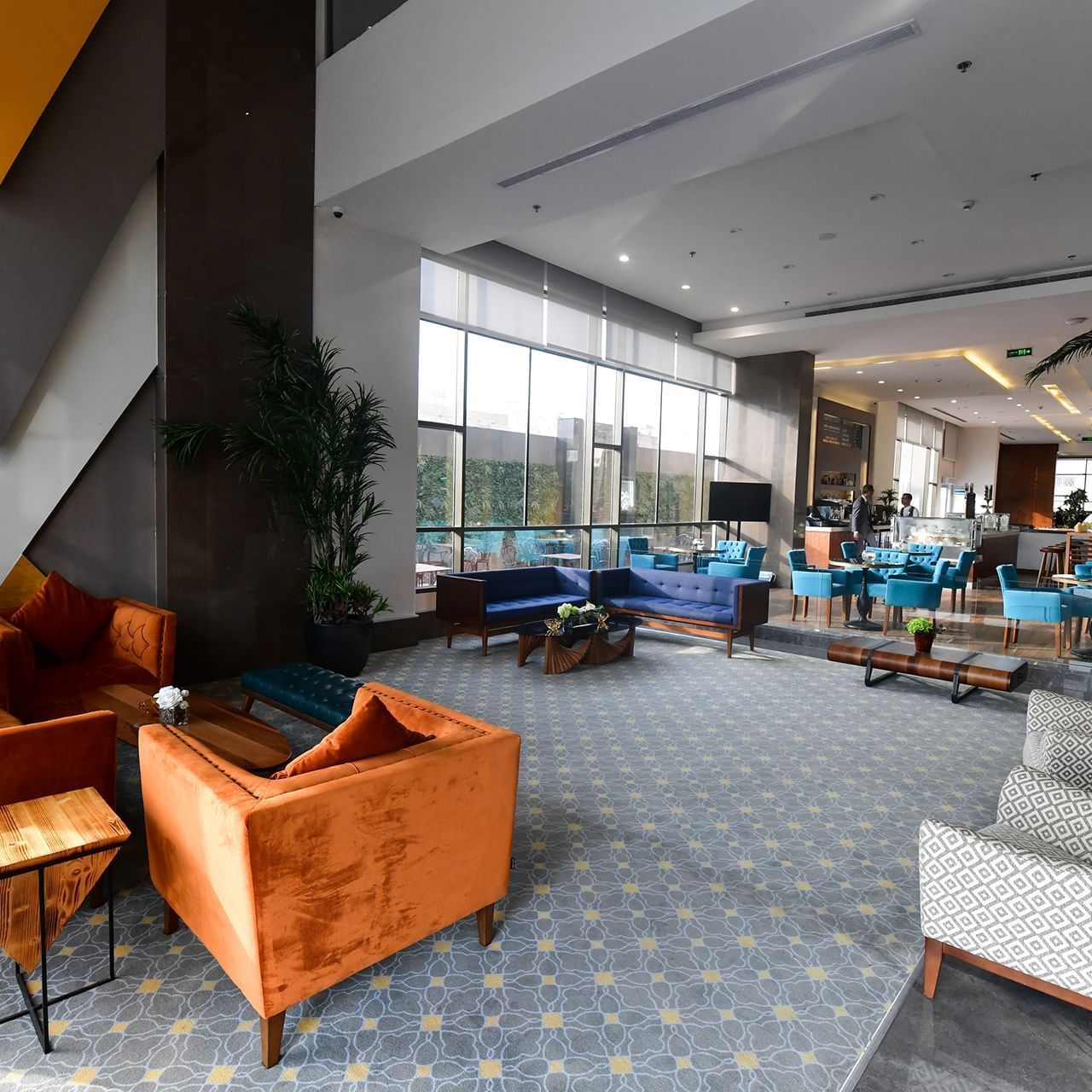 Des fauteuils orange et des canapés bleus entourent une table basse sous une grande baie vitrée dans le hall de l'hôtel Warwick de Djeddah