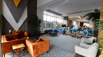 Orange armchairs by blue sofas surrounding a low table under a tall glass window in lobby at Warwick Hotel Jeddah
