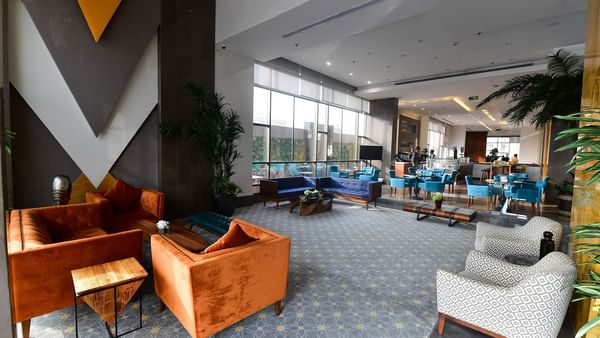 Orange armchairs by blue sofas surrounding a low table under a tall glass window in lobby at Warwick Hotel Jeddah