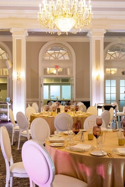 Round dining tables with gold cloths by white chairs under a grand chandelier at Rodd Charlottetown Hotel