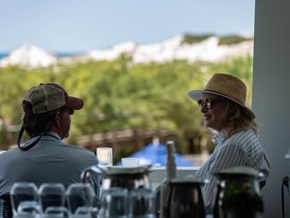 Two guests enjoying conversation at an outdoor terrace with scenic views of lush greenery and coastal buildings.