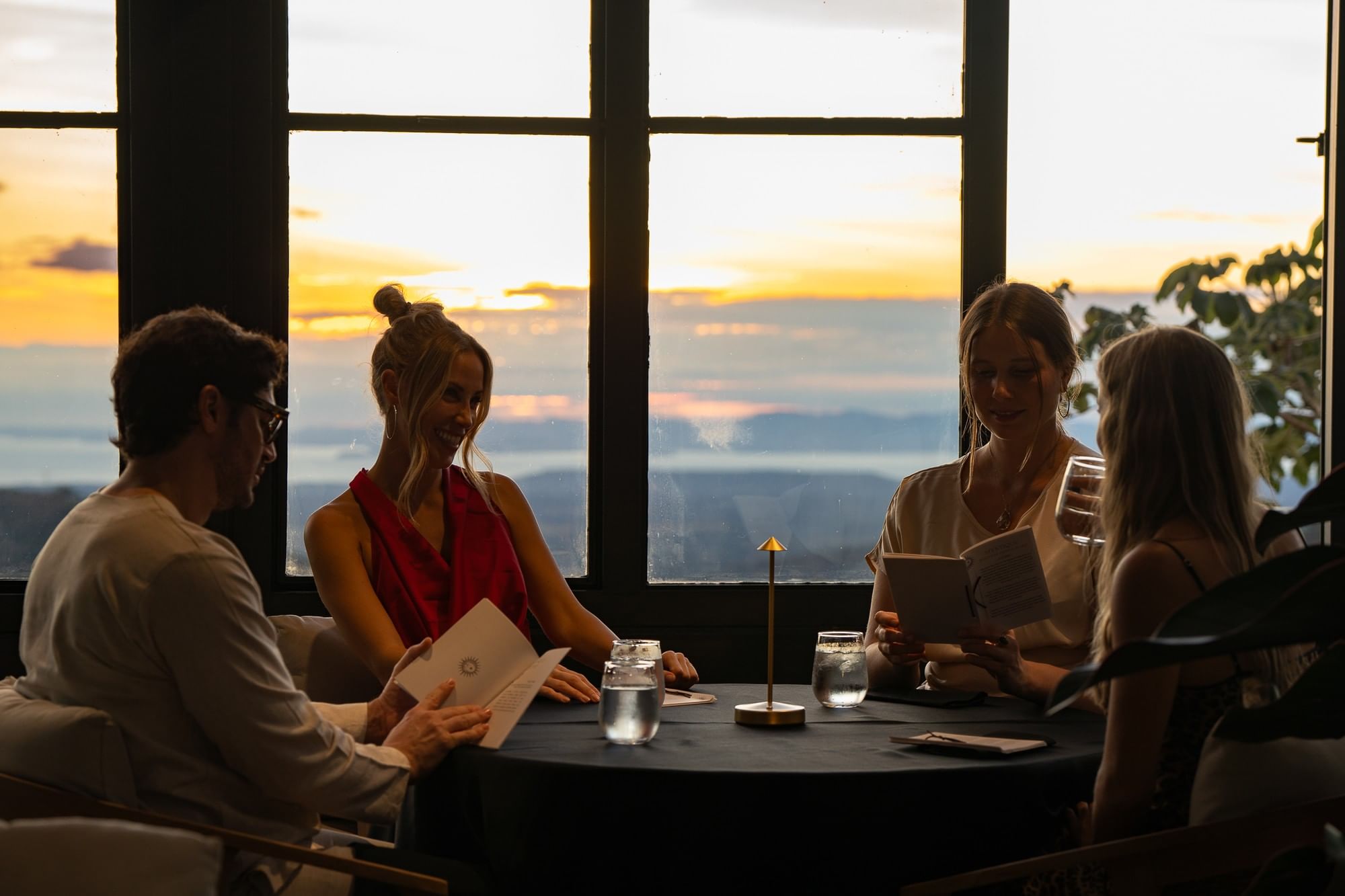 Huéspedes leyendo el menú al atardecer en el rooftop de Mystique, con las montañas y el cielo al fondo