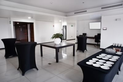 Event space in San Jose Costa Rica with tables, central wooden table, potted plant & buffet setup at D Sabana Hotel