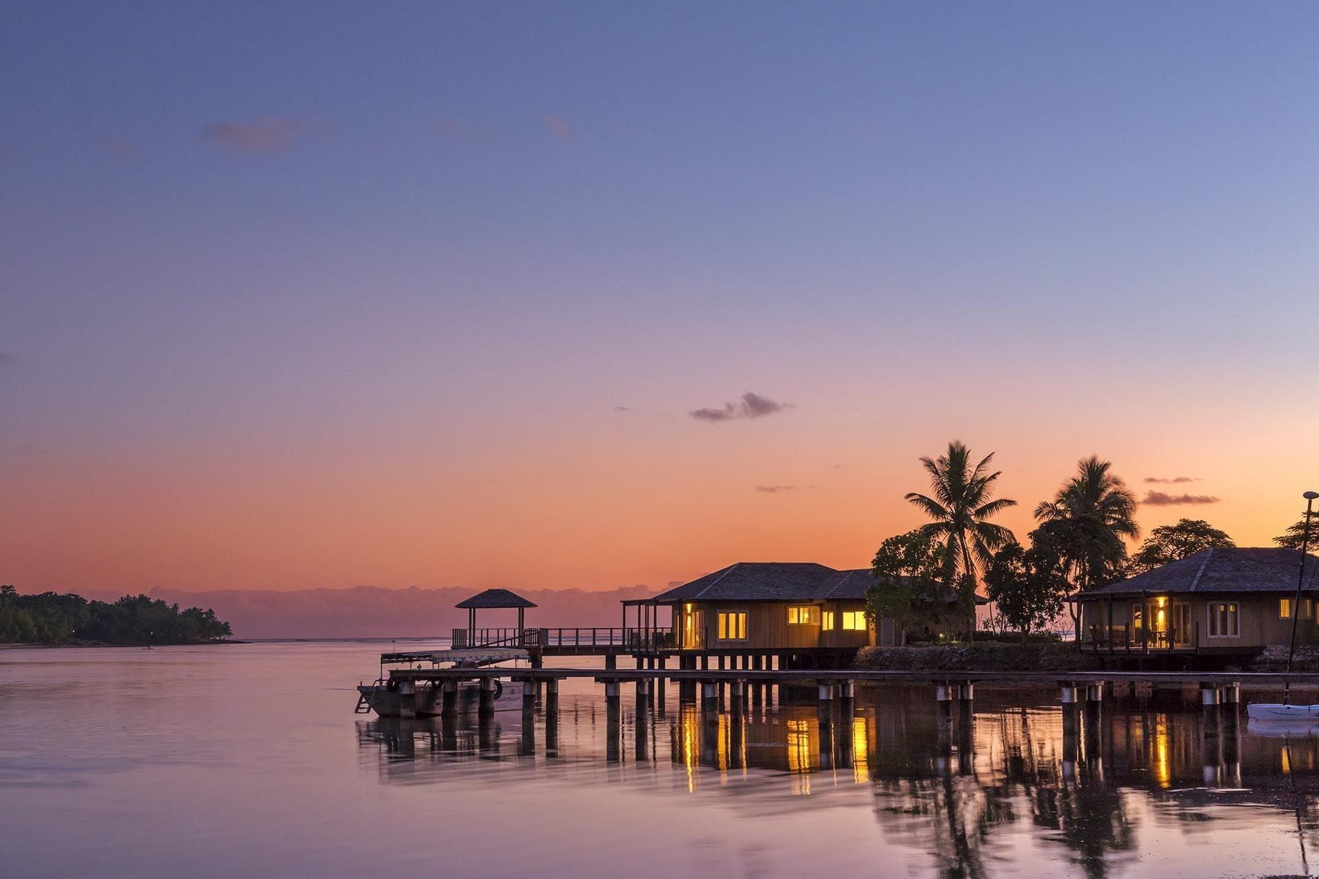 Overwater bungalows and a wooden pier reflect on calm water during a pink sunset at warwick le lagon-vanuatu