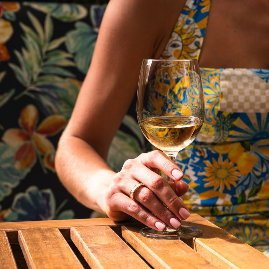 Close-up of a guest holding a glass of white wine at Riviera Hotel South Beach near a colorful floral pattern wall