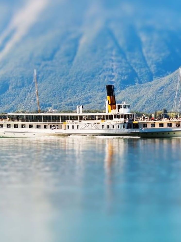 Lake Geneva with a steamship on a calm lake by blue mountains under a clear sky near Warwick Geneva