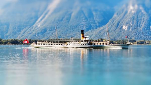 Lake Geneva with a steamship on a calm lake by blue mountains under a clear sky near Warwick Geneva