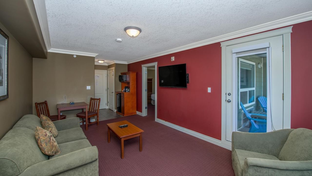 Coast Edson Hotel suite with red accent wall, green sofas, dining area, and balcony access.