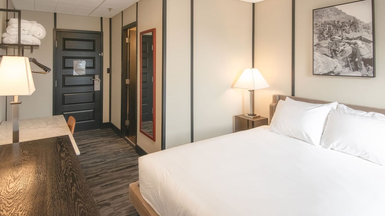 Hotel room with queen bed, night stand, lamp, and table
