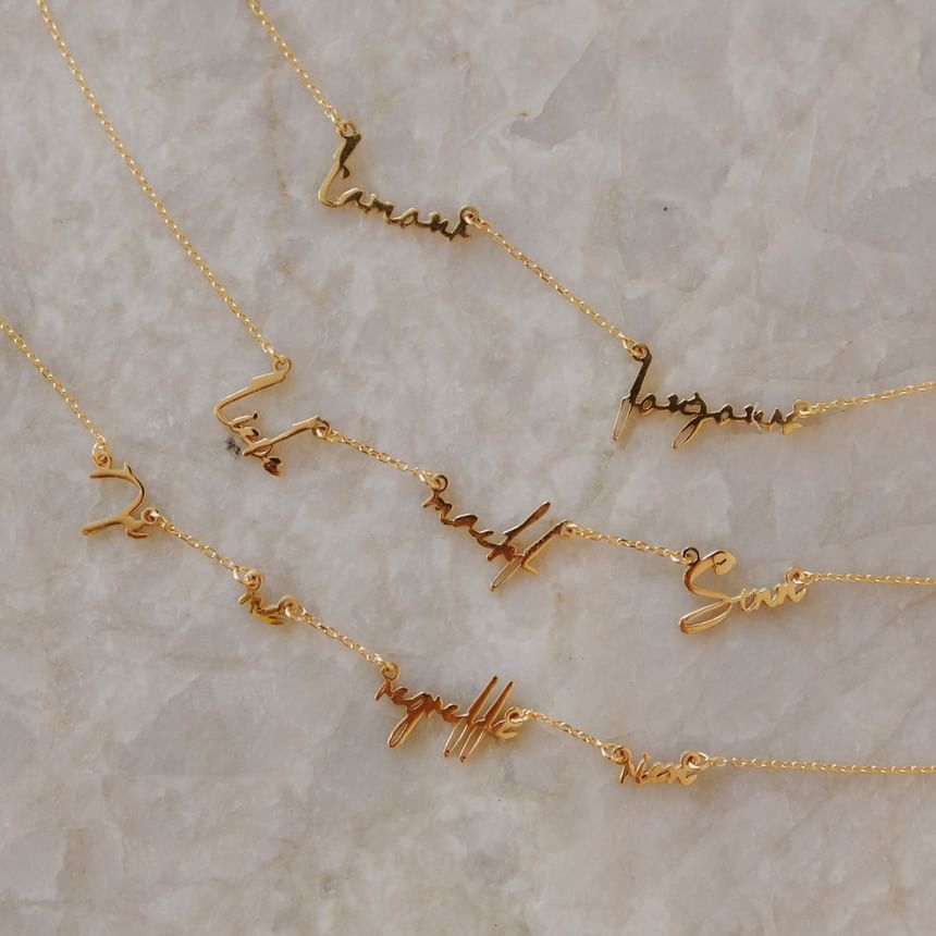 Fünf goldene Halsketten mit personalisierten Namen auf einem Marmorhintergrund fürs Hotel Motto