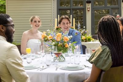 Bride and groom celebrating with guests at an elegant outdoor dining table with floral centerpiece at The Ashbrook Hotel