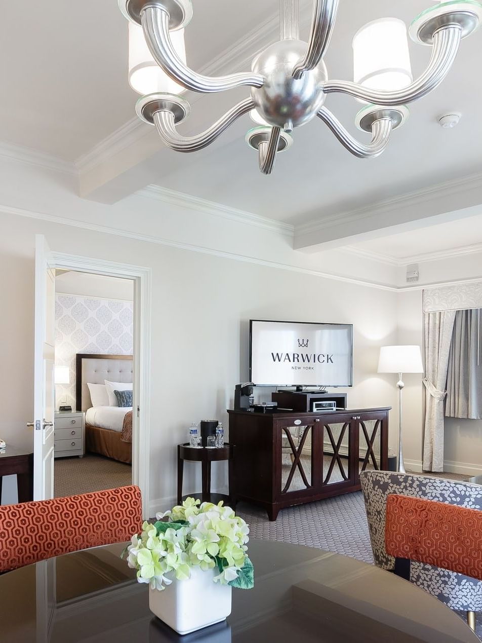 Silver chandelier & television, and dining furniture in the On the Avenue One Bedroom Suite at Warwick New York 