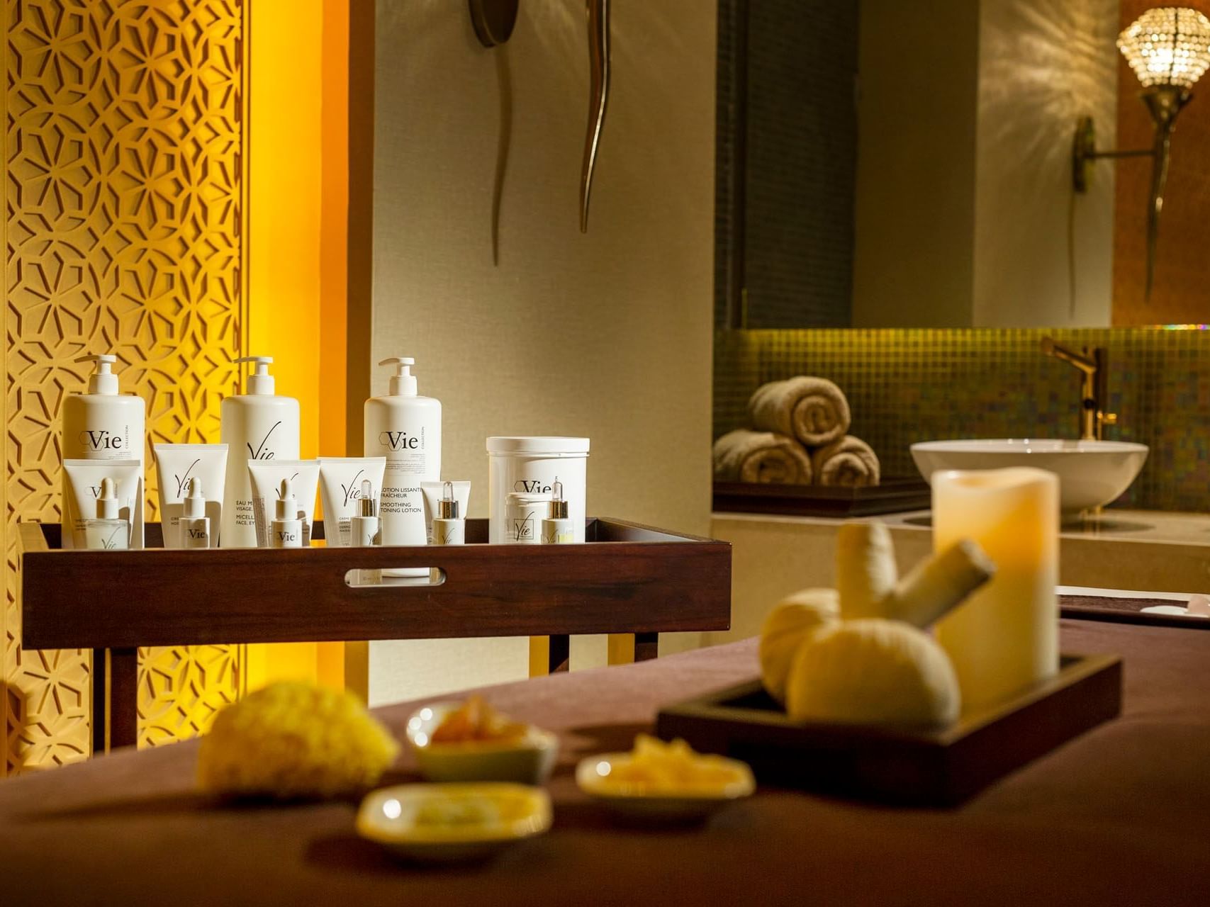 Spa treatment table with skincare products, candles, and massage tools set against a patterned wall.