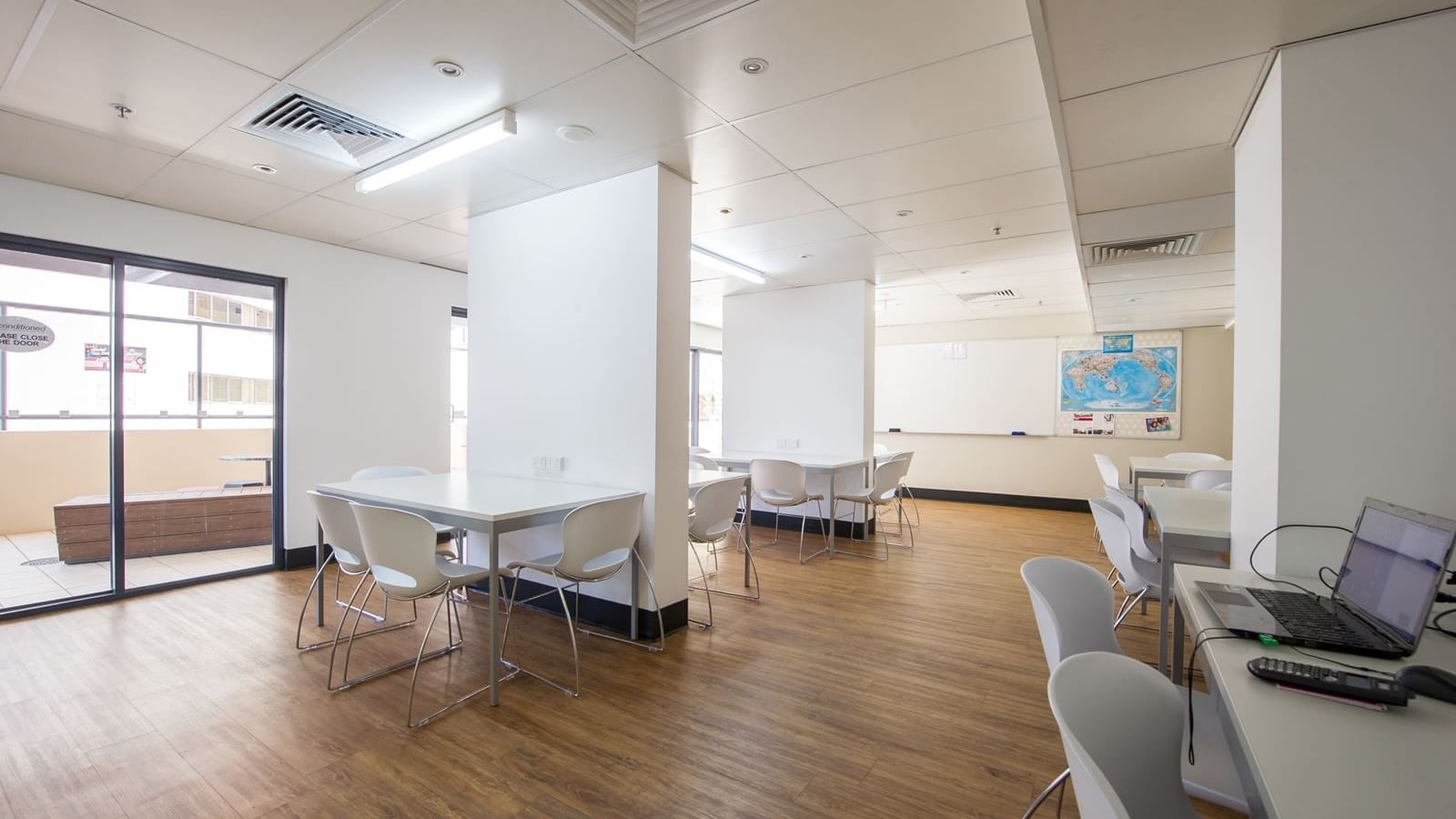 Modern communal study area with white tables, chairs, and wood flooring at StudentLiving - on Margaret