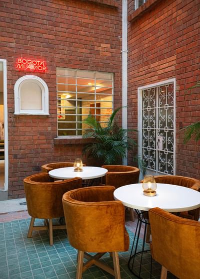 Courtyard with rust-colored brick walls, teal tiled floor, and velvet chairs at 5Q House, cheap hotels in Bogota Colombia