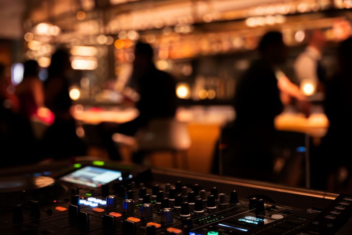 DJ mixer console in focus at May Fair Bar, with a blurred background showing silhouettes of people at The May Fair Hotel