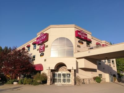 Exterior with a stone archway and large window beneath a bold red sign at Hilltop Inn Salmon Arm
