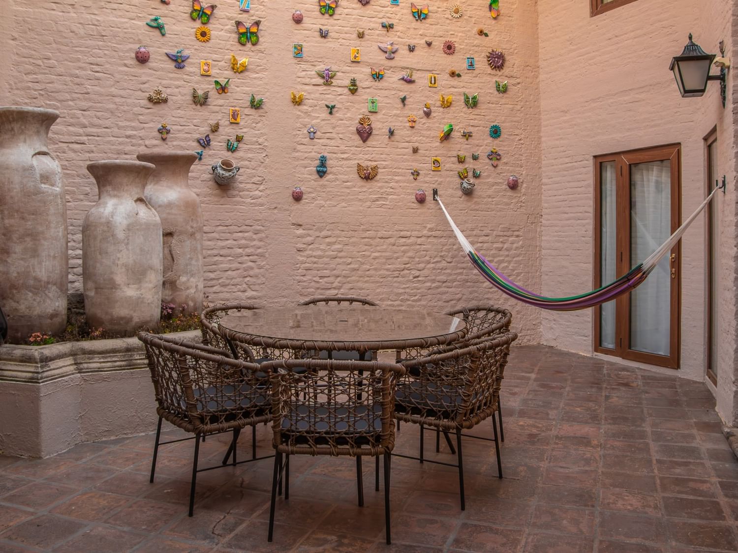 Patio privado con mesa de cristal, sillas de mimbre, hamaca y macetas decorativas en Quinta Real Guadalajara