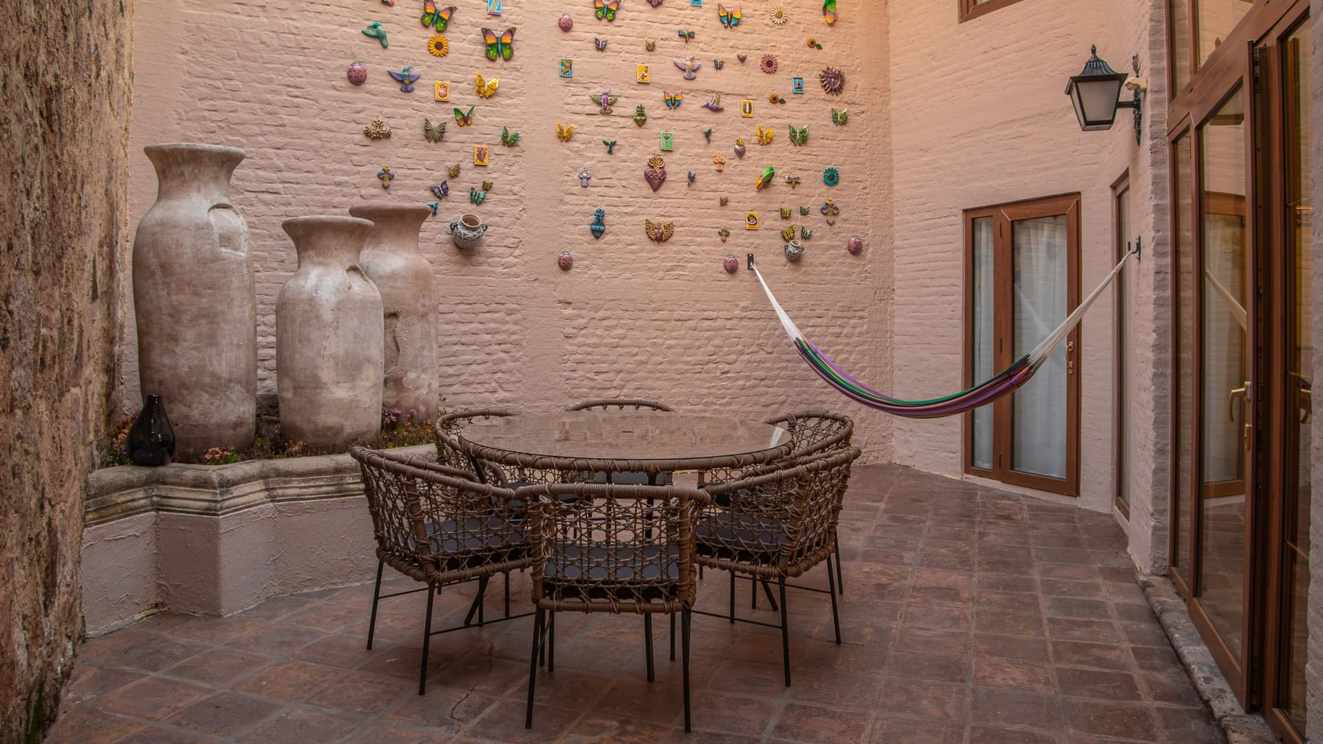 Patio privado con mesa de cristal, sillas de mimbre, hamaca y macetas decorativas en Quinta Real Guadalajara