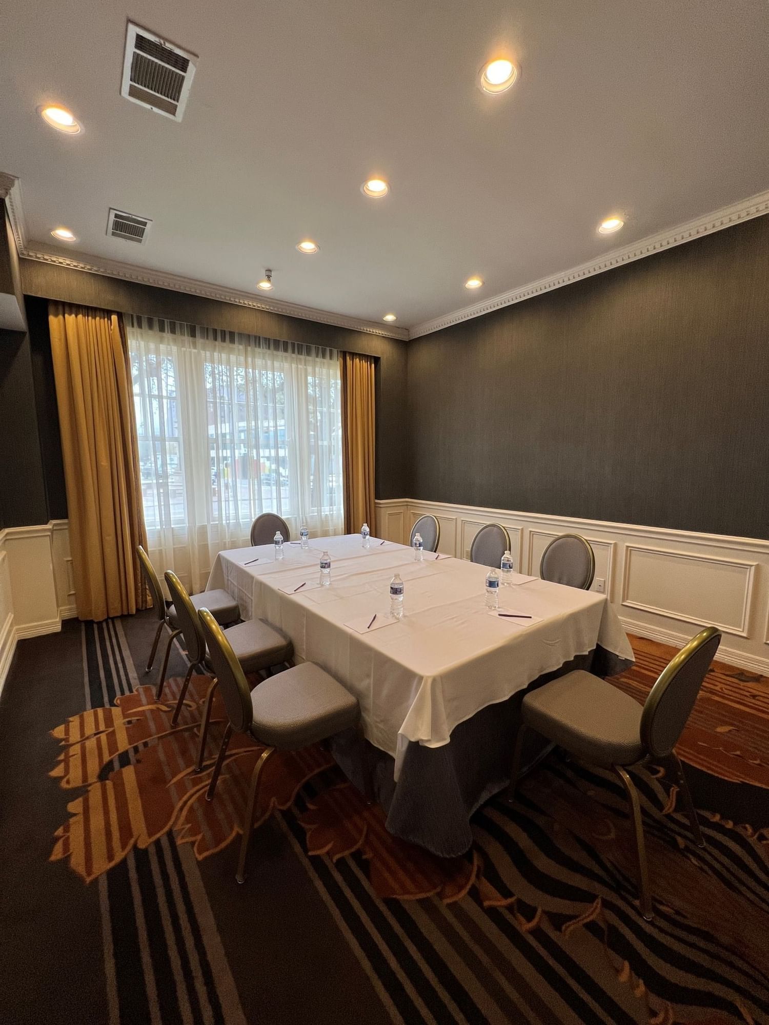 Meeting table with water bottles by grey chairs under recessed lights in Boardroom at Warwick Melrose Dallas
