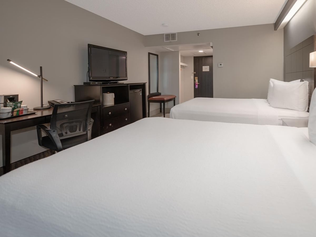 Two queen beds, desk, and TV in a hotel room.