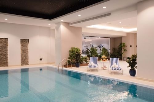 Indoor pool area with lounge chairs by a wall of plants under soft lights at Cantonal Hotel by Warwick Riyadh