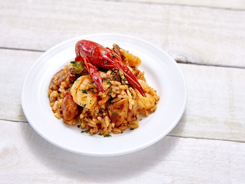 A white bowl of jambalaya topped with a red crawfish on a white wooden background. 